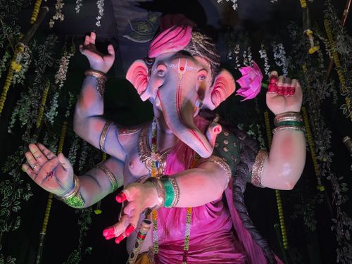 Free Colorful statue of Lord Ganesha in traditional attire, with vibrant pink and green highlighted details, surrounded by floral decor. Stock Photo