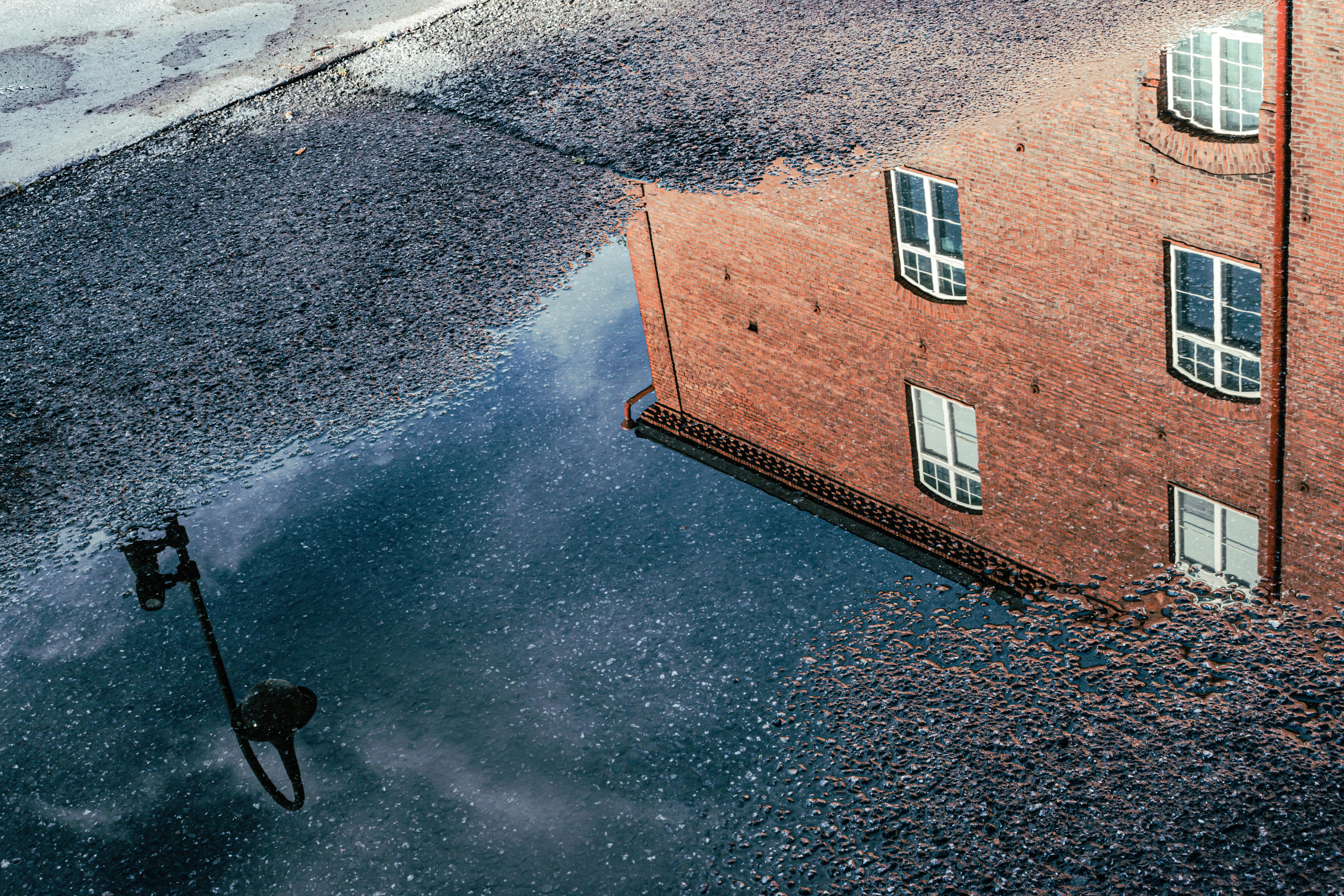 Stunning reflection of a brick building and lamp post in a puddle in Tampere, showcasing unique urban artistry. - Tampere