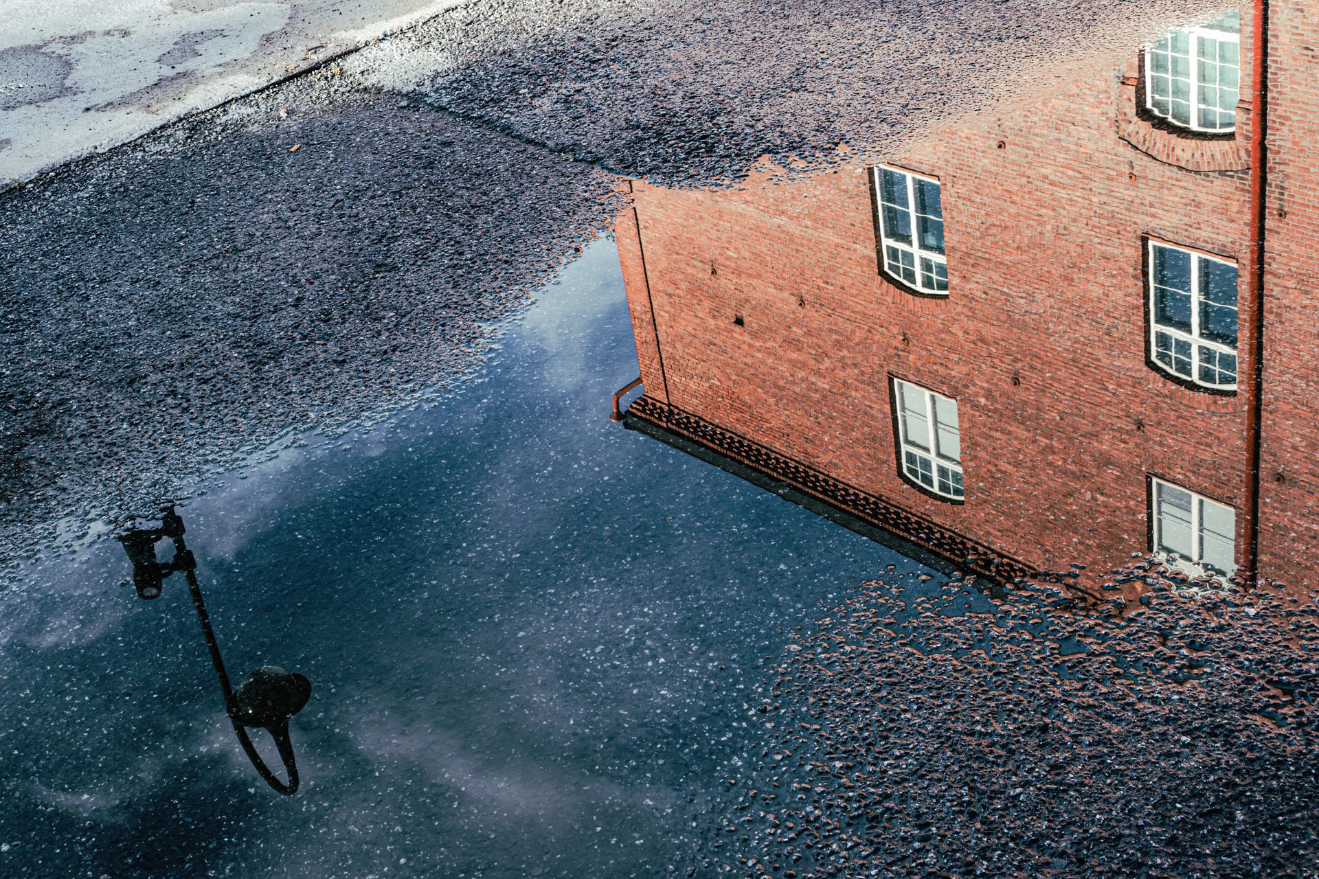 Stunning reflection of a brick building and lamp post in a puddle in Tampere, showcasing unique urban artistry.
