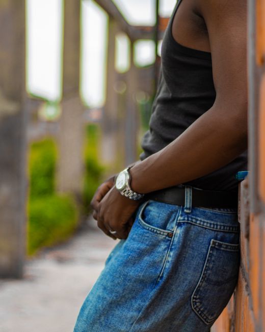 Man in black tank top and jeans leaning outdoors, casual style. Man in black tank top and jeans leaning outdoors, casual style.