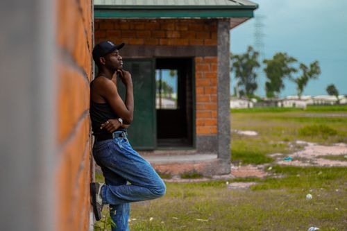 Free Young man in casual attire leaning on a brick wall, pondering deeply outdoors. Stock Photo