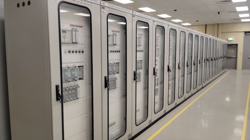 Row of enclosed electrical switchgear cabinets receding down an industrial corridor