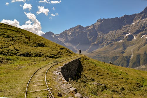 Grey Railway Near Green Grassy Hill during Cloudy Day