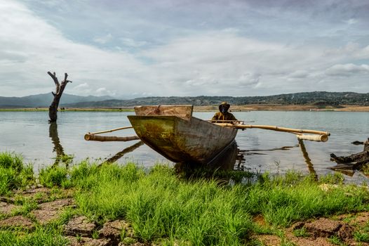 A traditional fisherman in an outrigger boat on Pantabangan Lake with scenic mountainous backdrop.