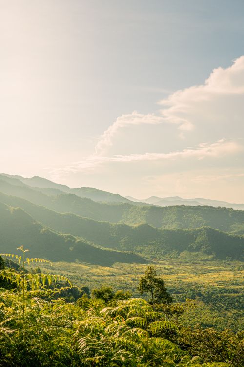 Free Beautiful sunlit view of lush green mountains under a bright sky with soft clouds. Stock Photo