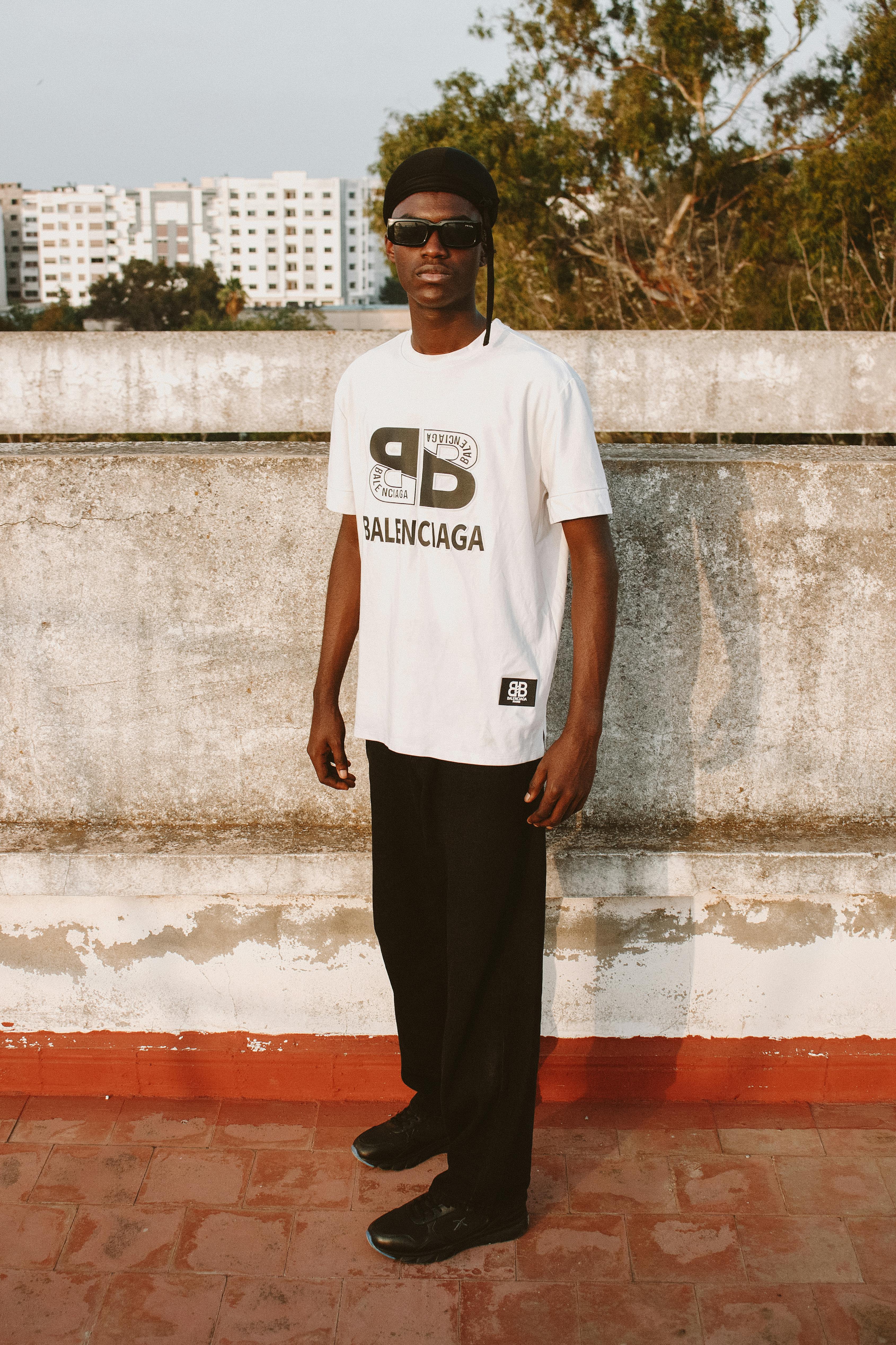 A fashionable young man in a branded shirt poses outdoors in Morocco.