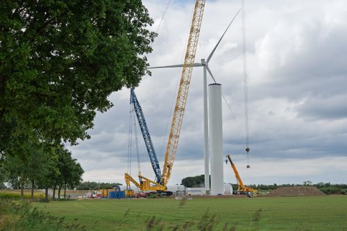 Free Cranes assembling a wind turbine in a grassy field under a cloudy sky. Stock Photo