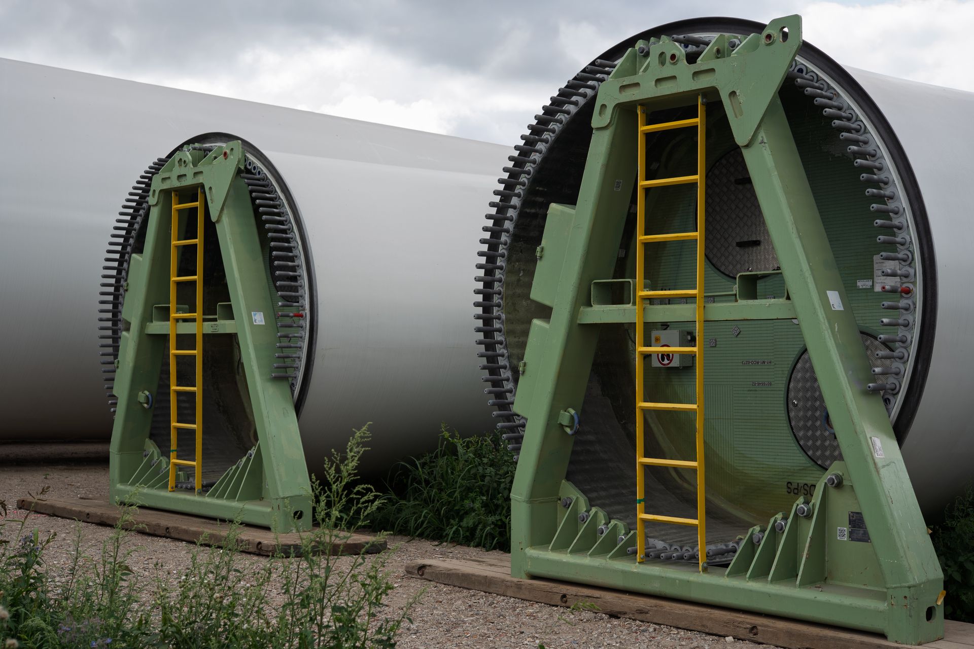 Close-up view of large wind turbine blades supported by metal racks in an outdoor setting, showcasing renewable energy equipment.