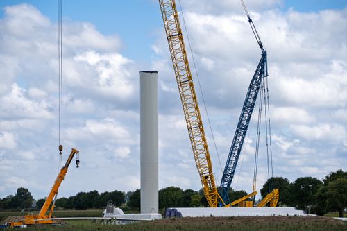 Free Cranes assembling a wind turbine tower in an open field under a cloudy sky. Stock Photo