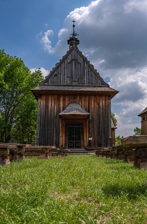 Free A rustic wooden chapel with a historical charm stands surrounded by greenery and under a partly cloudy sky, evoking a serene atmosphere. Stock Photo