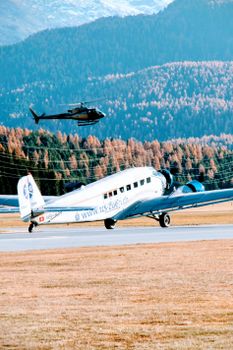 A vintage plane and helicopter flying over the scenic Swiss Alps landscape.