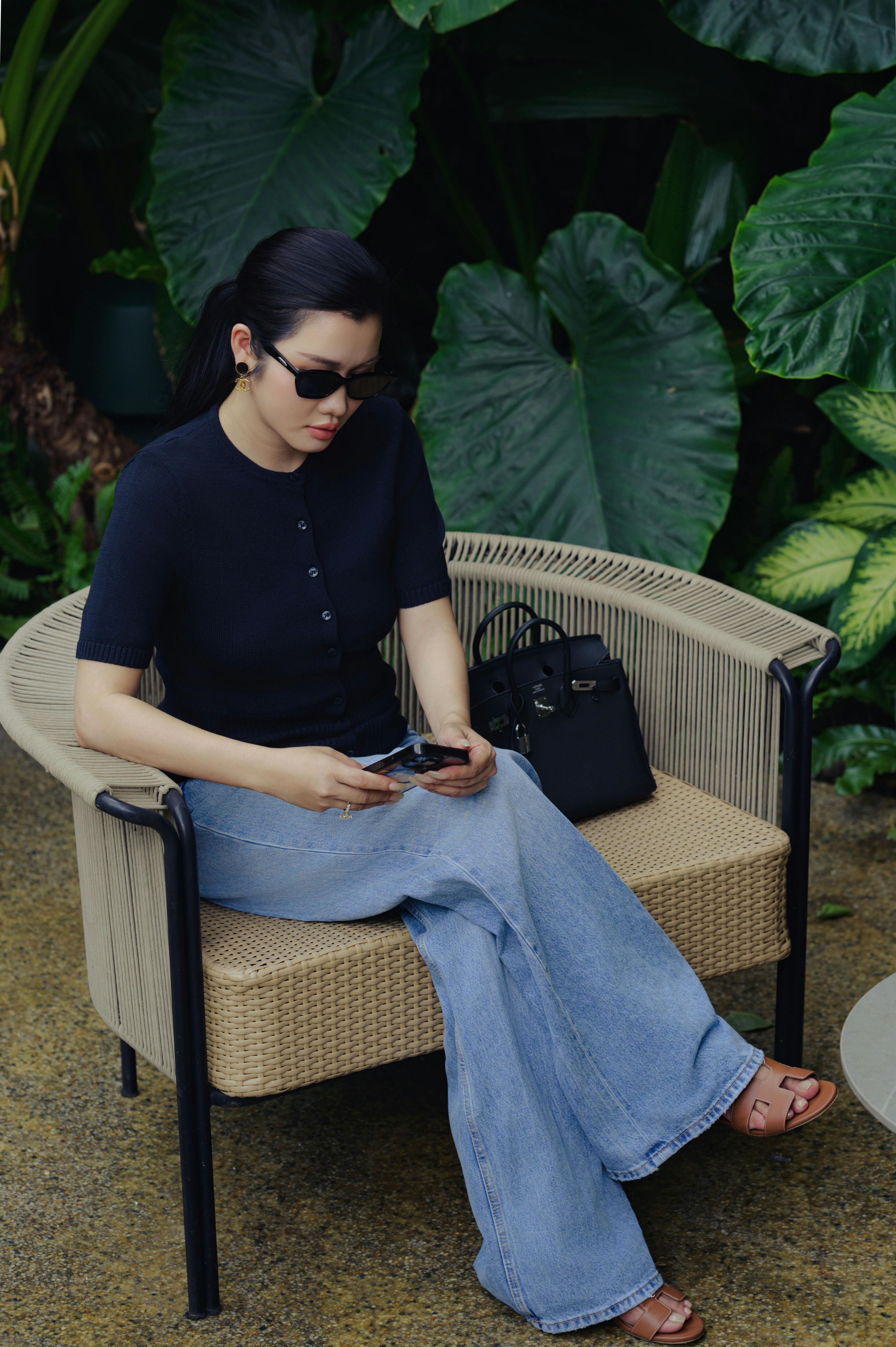 Elegantly dressed woman sitting outdoors in a lush garden setting.