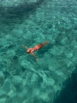 Woman floating in serene turquoise sea water, enjoying a sunny day.