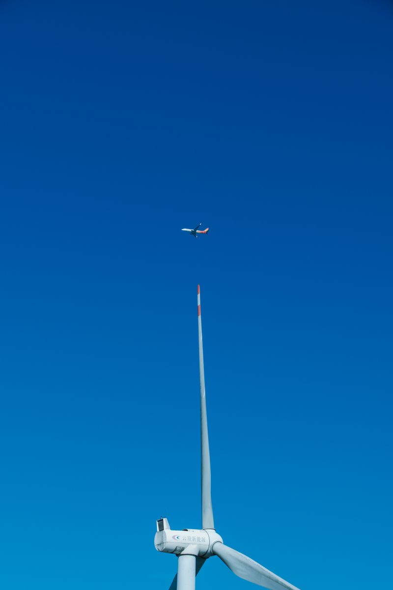 Wind turbine generating clean electricity with a commercial jet flying above, symbolizing the goal of green aviation powered by renewable energy
