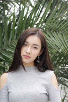 一位穿着休闲装的时尚年轻女子，在棕榈叶的衬托下于户外摆着姿势