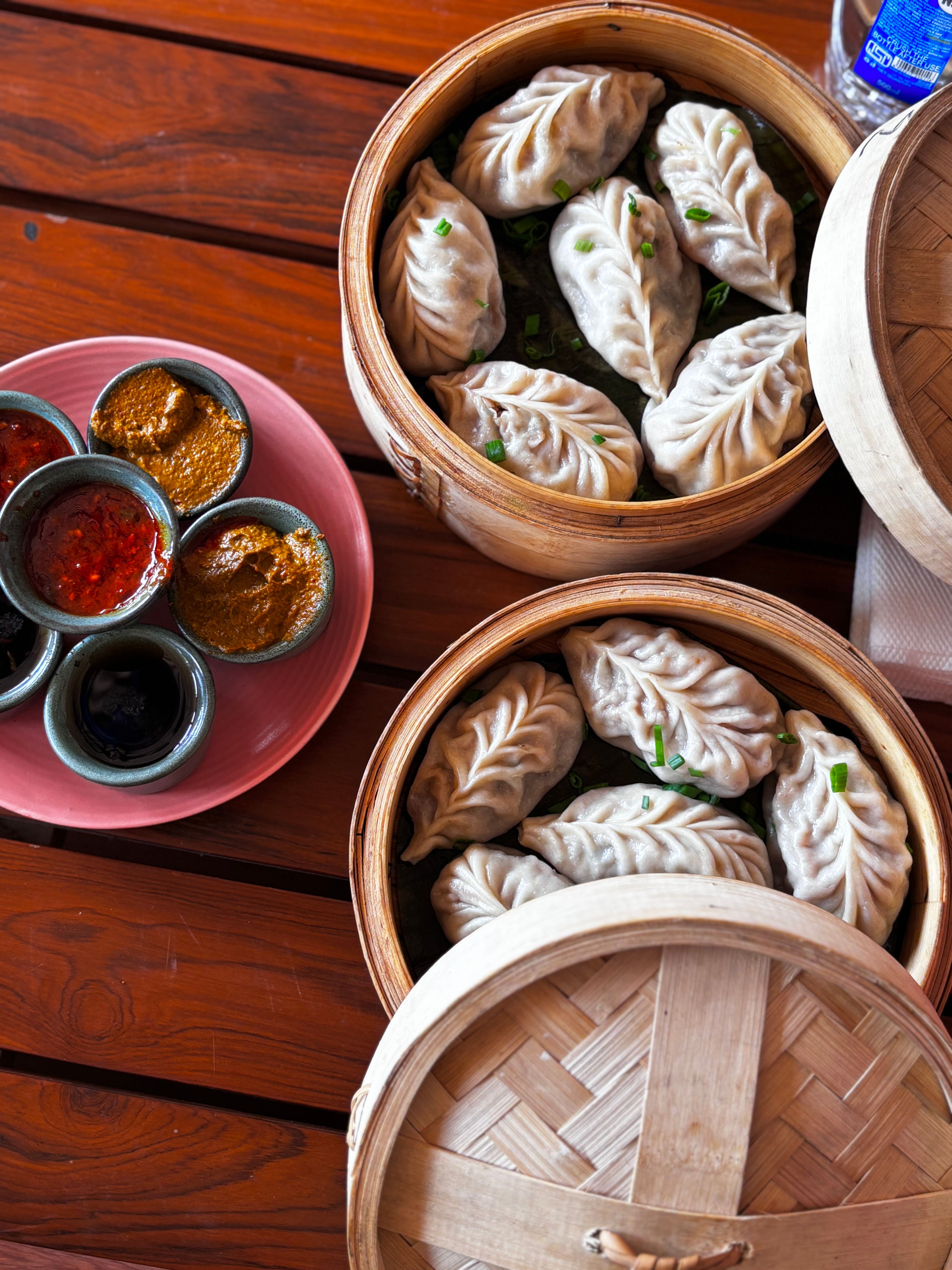 Top view of steamed dumplings in bamboo baskets with various Asian dipping sauces on a rustic table.