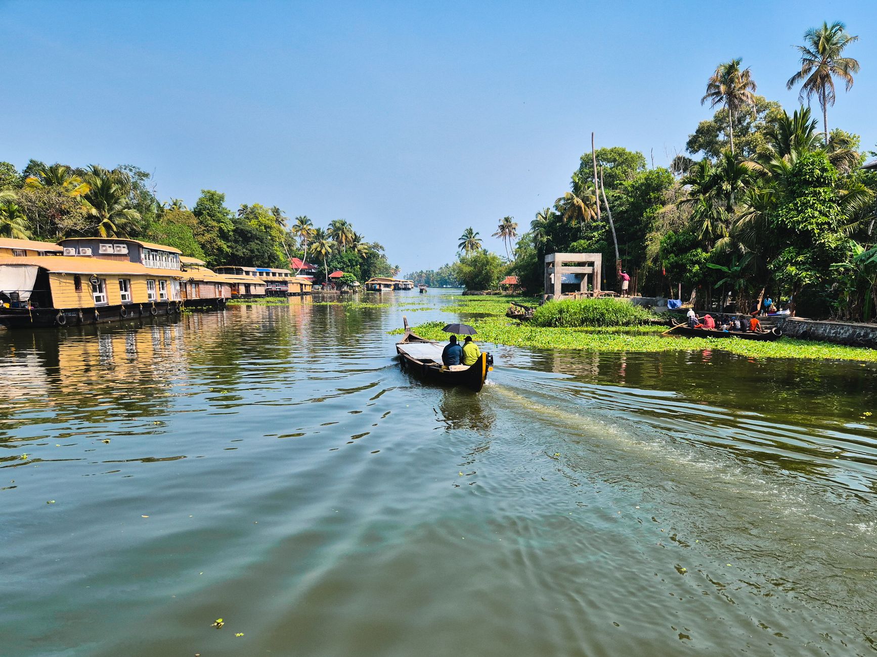 Kerala houseboat moving through Vembanad Lake backwaters with palm trees and golden morning light