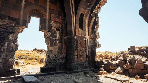 An artistic view of ancient stone ruins featuring a desolate archway under a clear blue sky.