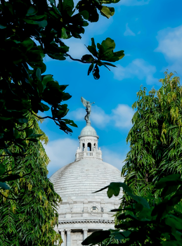 The iconic dome of Victoria Memorial in Kolkata, framed by verdant trees under a vibrant blue sky.