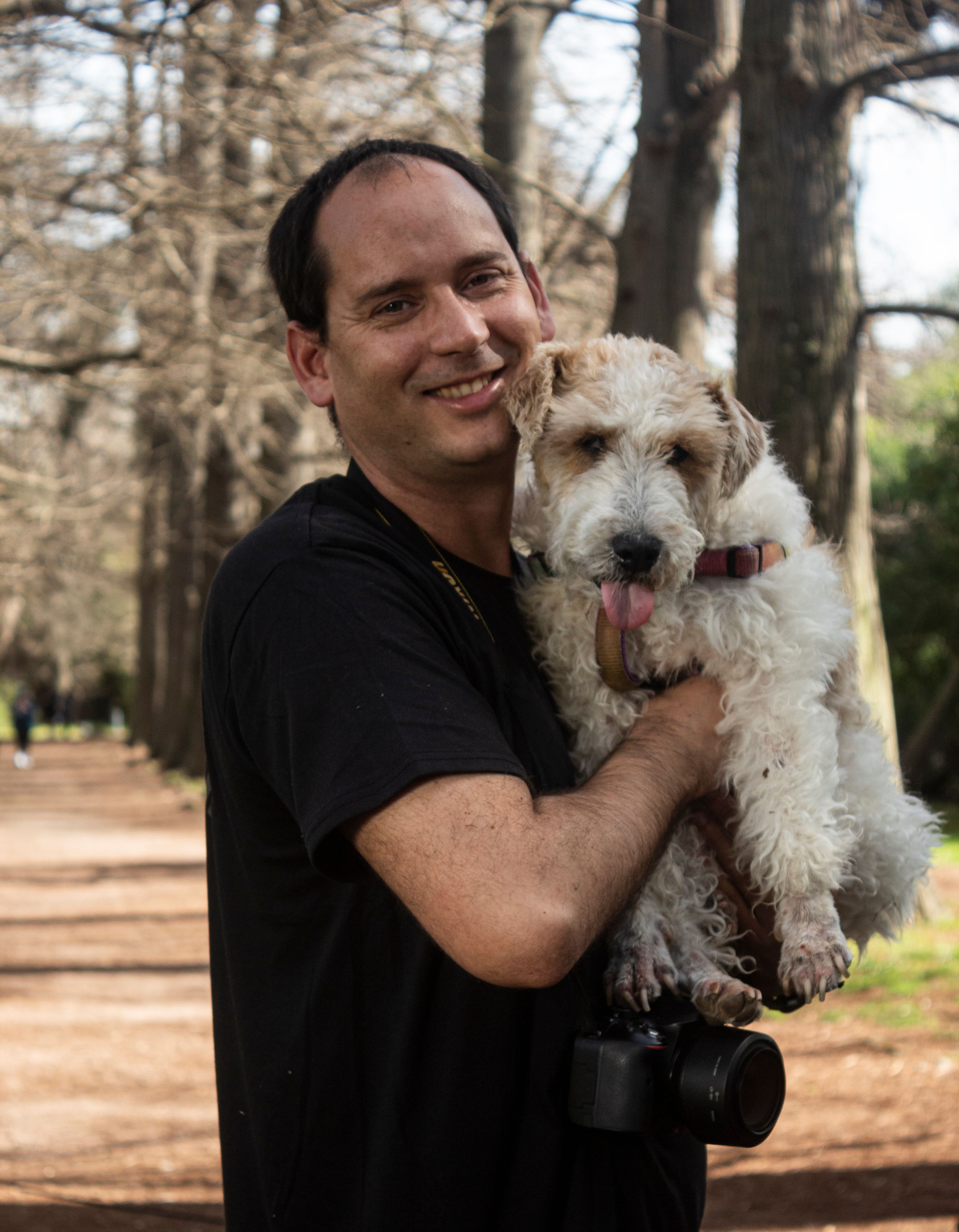 Man holding a dog in a sunlit Montevideo park, capturing joy and companionship.