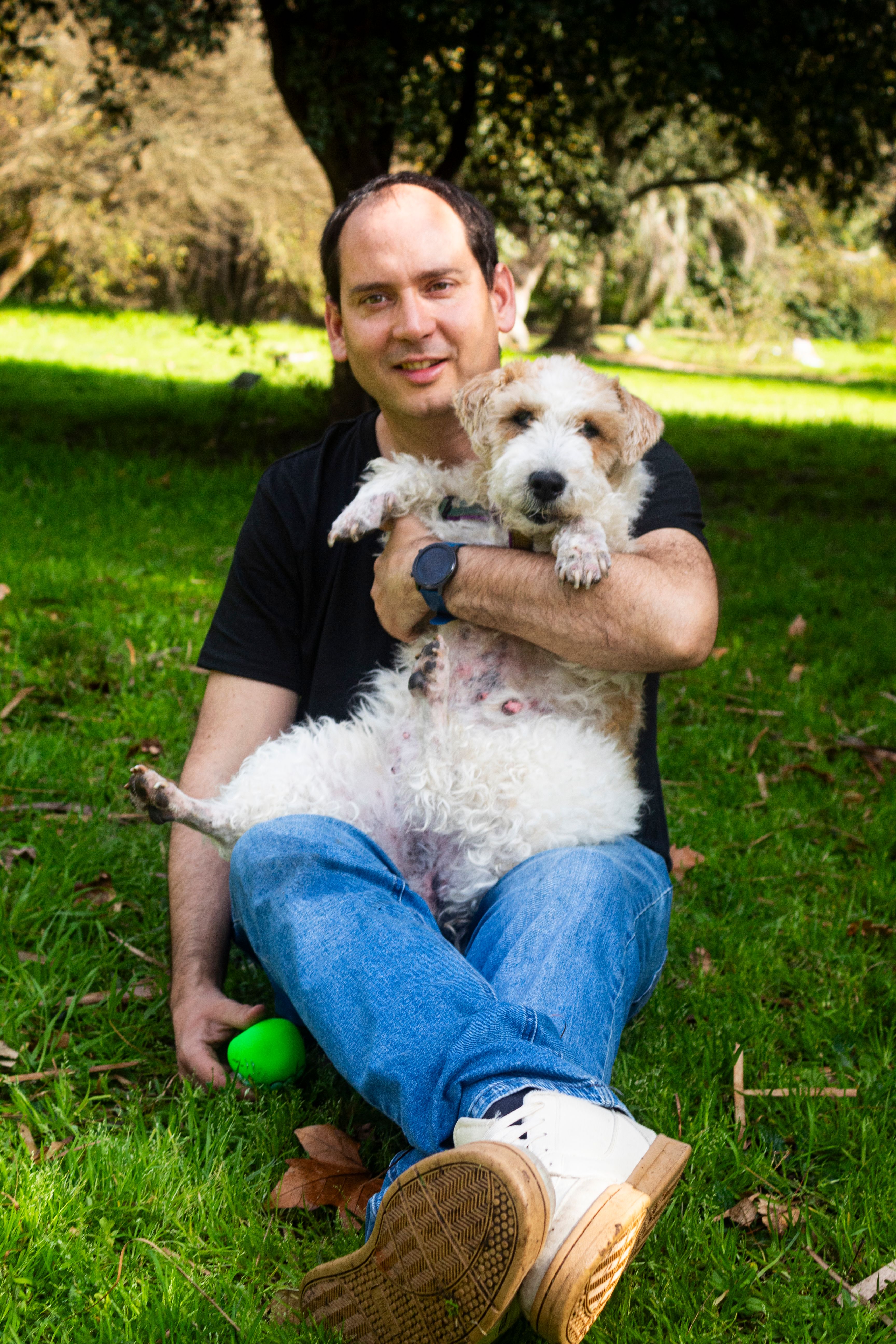 A man sitting on grass with his terrier dog in Montevideo, Uruguay.
