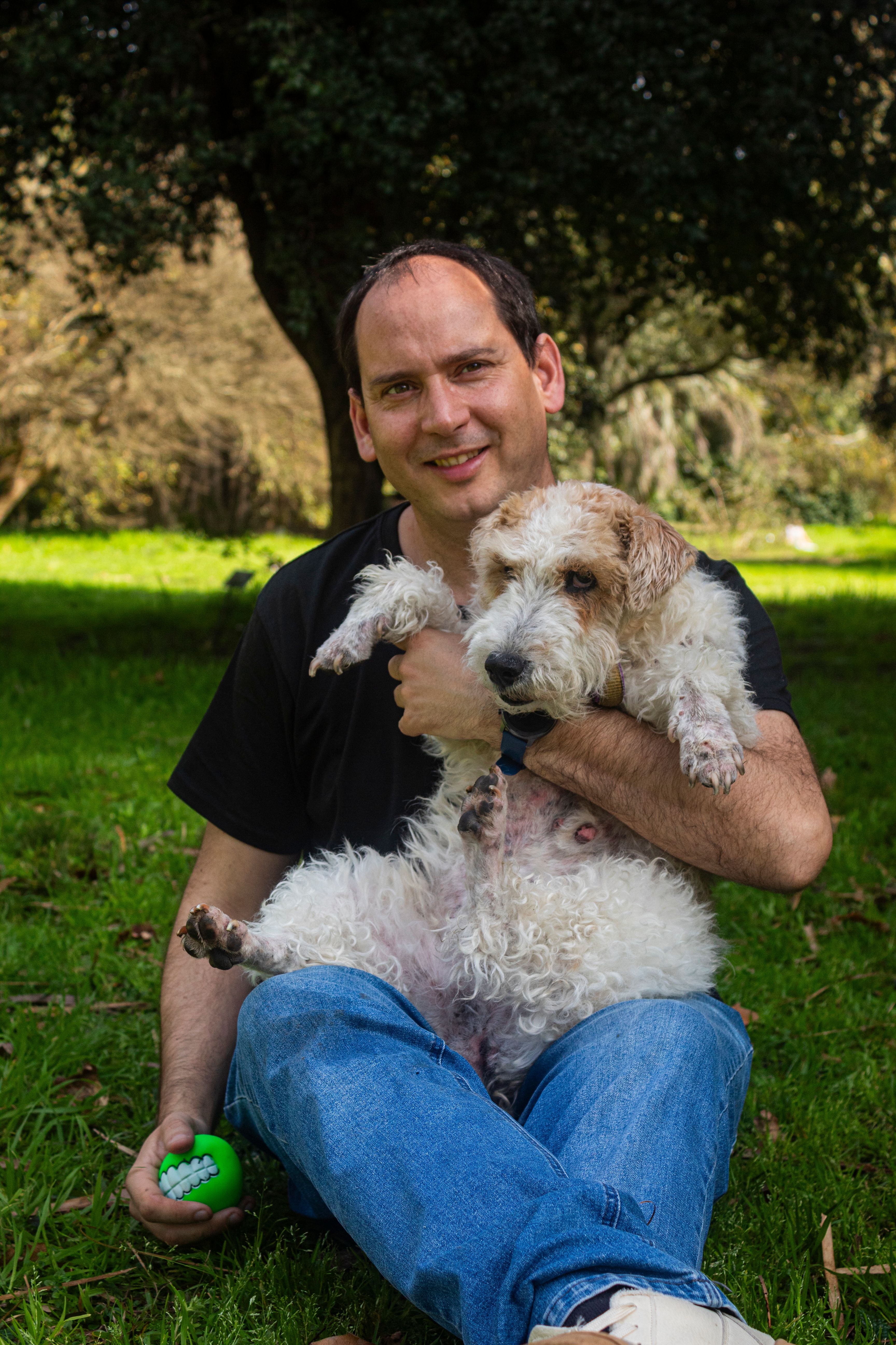 A man sitting outdoors in a park holding a dog and enjoying a sunny day in Montevideo, Uruguay.
