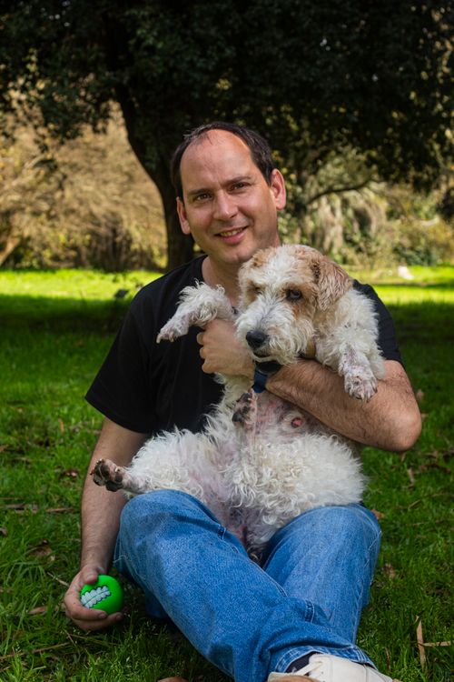 Free A man sitting outdoors in a park holding a dog and enjoying a sunny day in Montevideo, Uruguay. Stock Photo