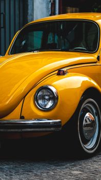Close-up of a vintage yellow car parked on a cobblestone street. Classic feel.