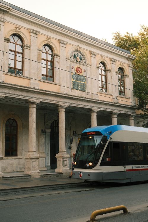 Free A contemporary tram travels past a historic building on a sunny day, blending modernity with history. Stock Photo