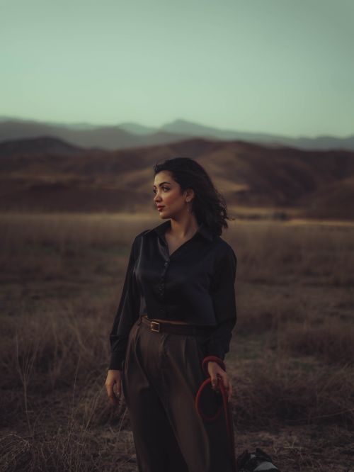 Free A woman in elegant attire stands in a tranquil mountain landscape at dusk, evoking a sense of calm and introspection. Stock Photo