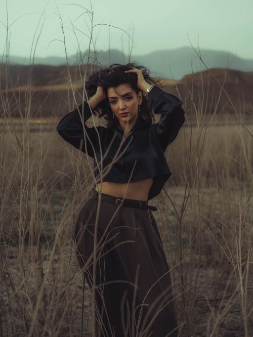 Free Woman in black top and brown skirt posing in a tranquil dry field with mountains in the background. Stock Photo