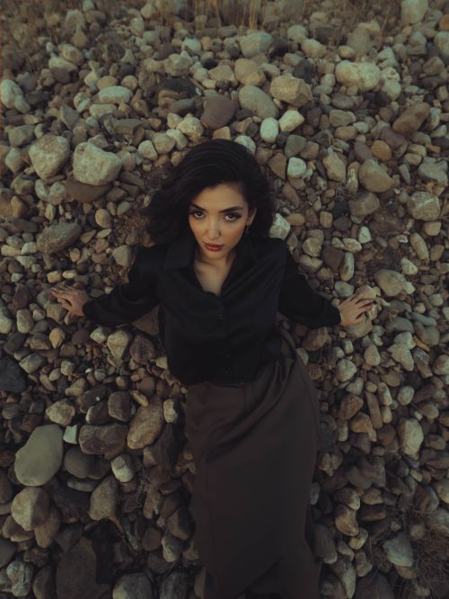 Free A stylish woman in dark attire lies gracefully on a rocky surface, evoking a sense of mystery. Stock Photo