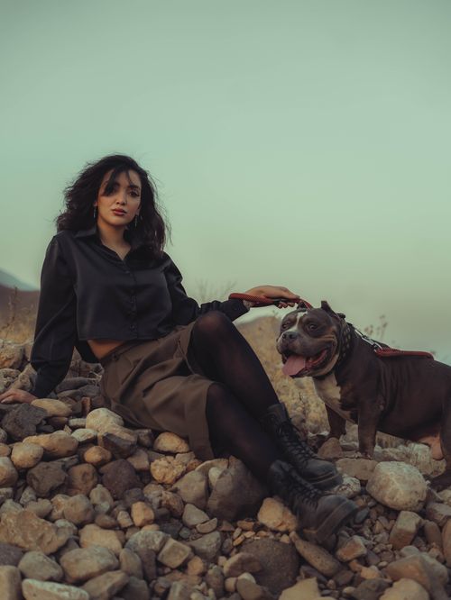 Free A woman sits with her Pit Bull on a rocky hillside during dusk, exuding calmness. Stock Photo