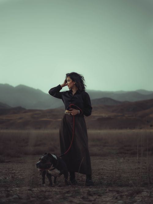 Free Woman with dog on leash standing in mountain scenery during twilight, evoking calm and introspection. Stock Photo