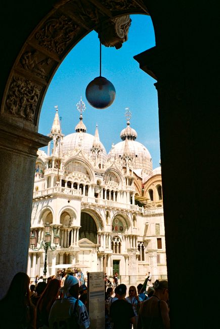 Beautiful view of St. Mark's Basilica in Venice captured through an archway with a clear blue sky.