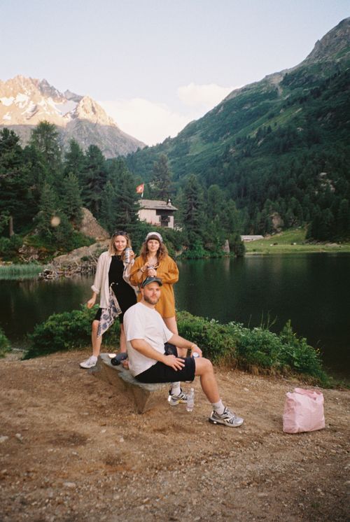 Free Three friends enjoying a scenic view by a mountain lake, capturing a serene summer moment. Stock Photo