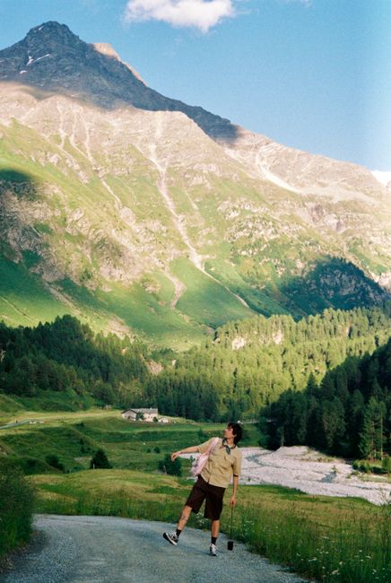 A hiker joyfully explores a lush mountain landscape under a bright summer sky.