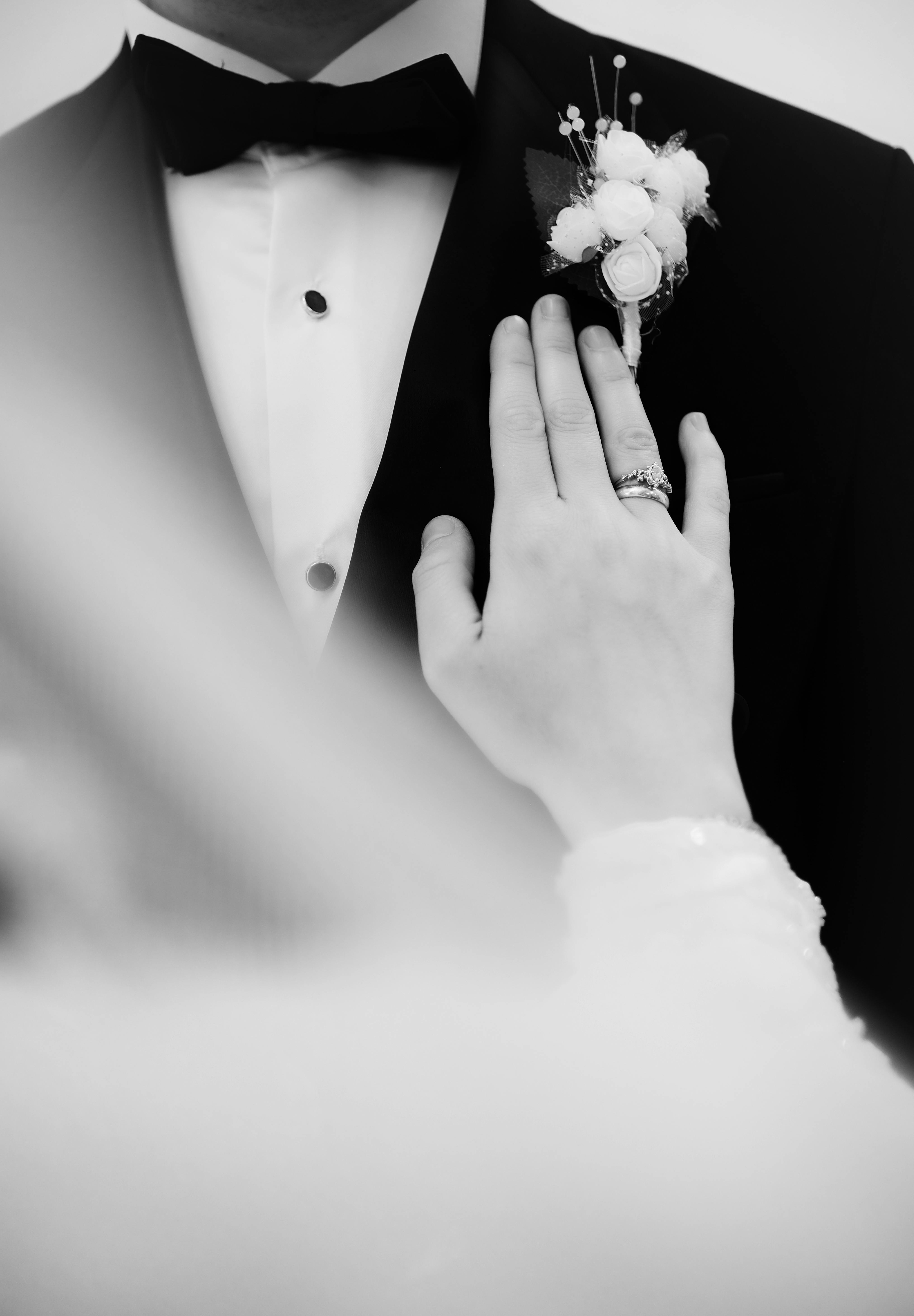 免費 新娘的手放在新郎禮服上的特寫鏡頭，禮服上有黑白相間的胸花。 圖庫相片