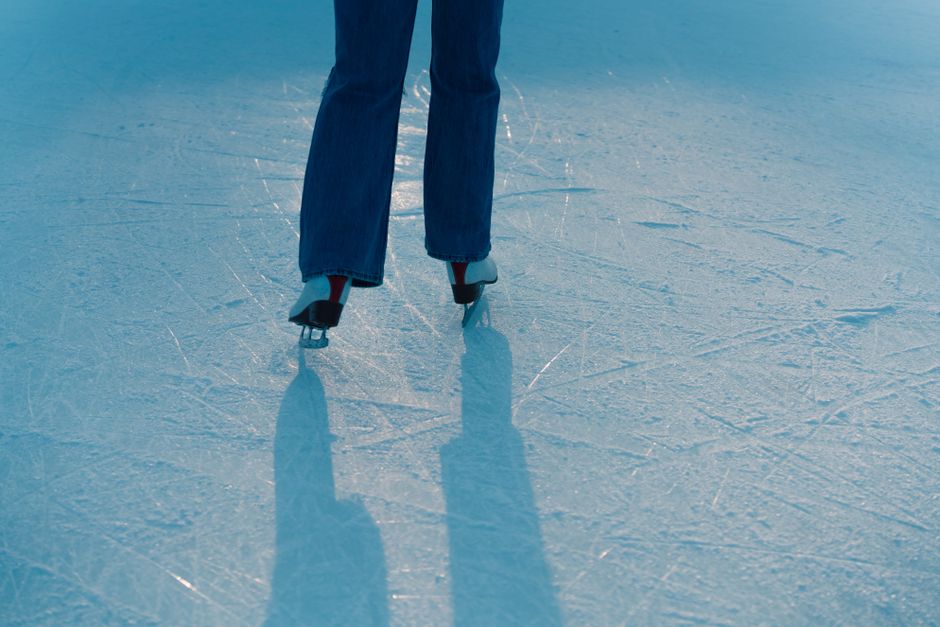 Rear view of individual ice skating on a textured rink with shadows cast in sunlight.