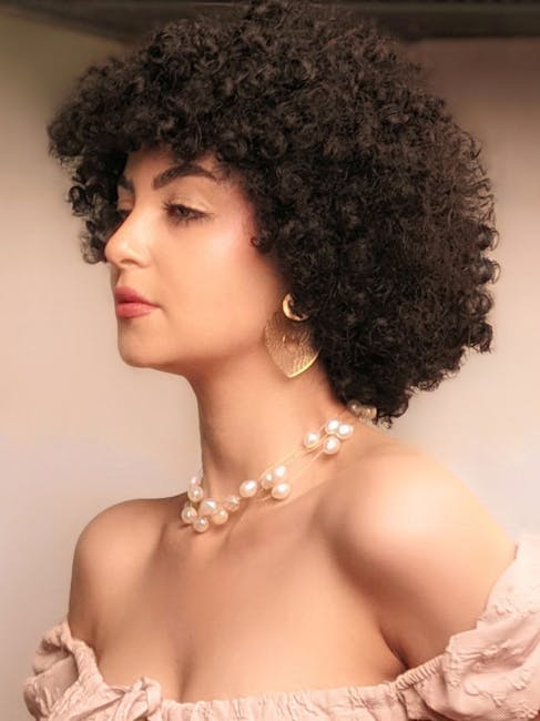 Profile portrait of an elegant woman with curly hair, wearing pearl jewelry.