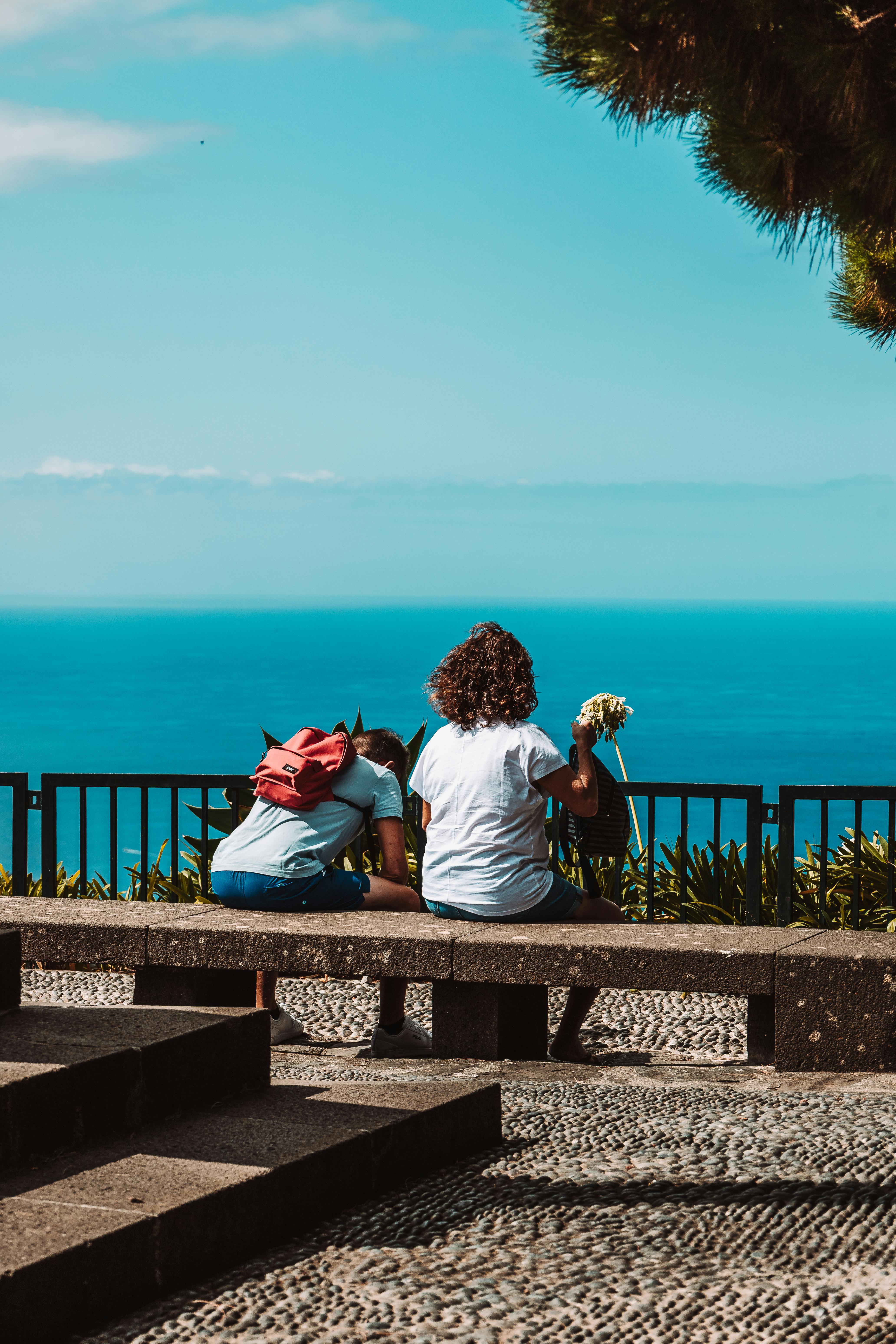 People sitting on a bench looking over Madeira oceanfront