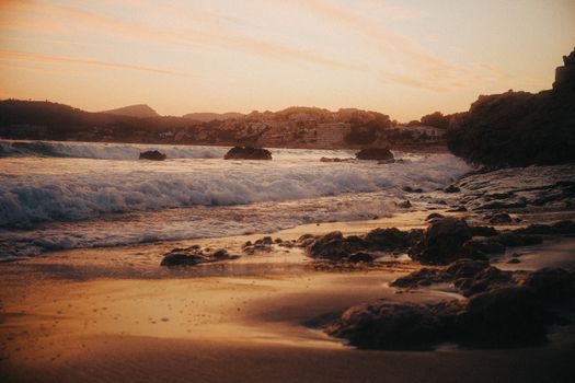 Beautiful coastal sunset with waves crashing on a rocky shoreline, creating a peaceful and dramatic scene.