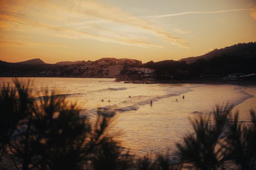 Surfers enjoying gentle waves at a Mediterranean beach during a stunning sunset view.