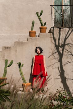 Stylish portrait of a woman in red dress in front of Mexican architecture with cacti.