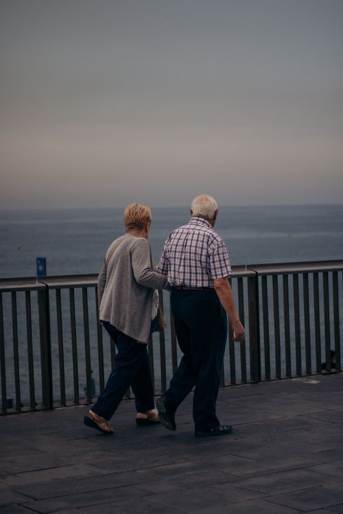 Free An elderly couple strolls along an oceanside boardwalk, embracing serene companionship. Stock Photo