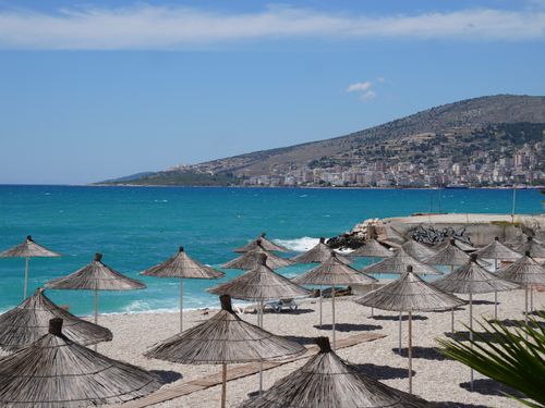 Free Scenic Mediterranean beach with umbrellas and city backdrop, perfect for summer travel. Stock Photo
