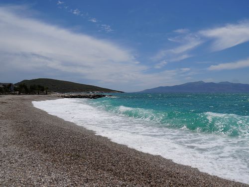 Free Tranquil pebble beach with turquoise waves and clear skies, ideal for relaxation. Stock Photo