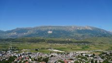 Scenic view of Gjirokaster city with mountains, showcasing lush greenery and clear blue skies.
