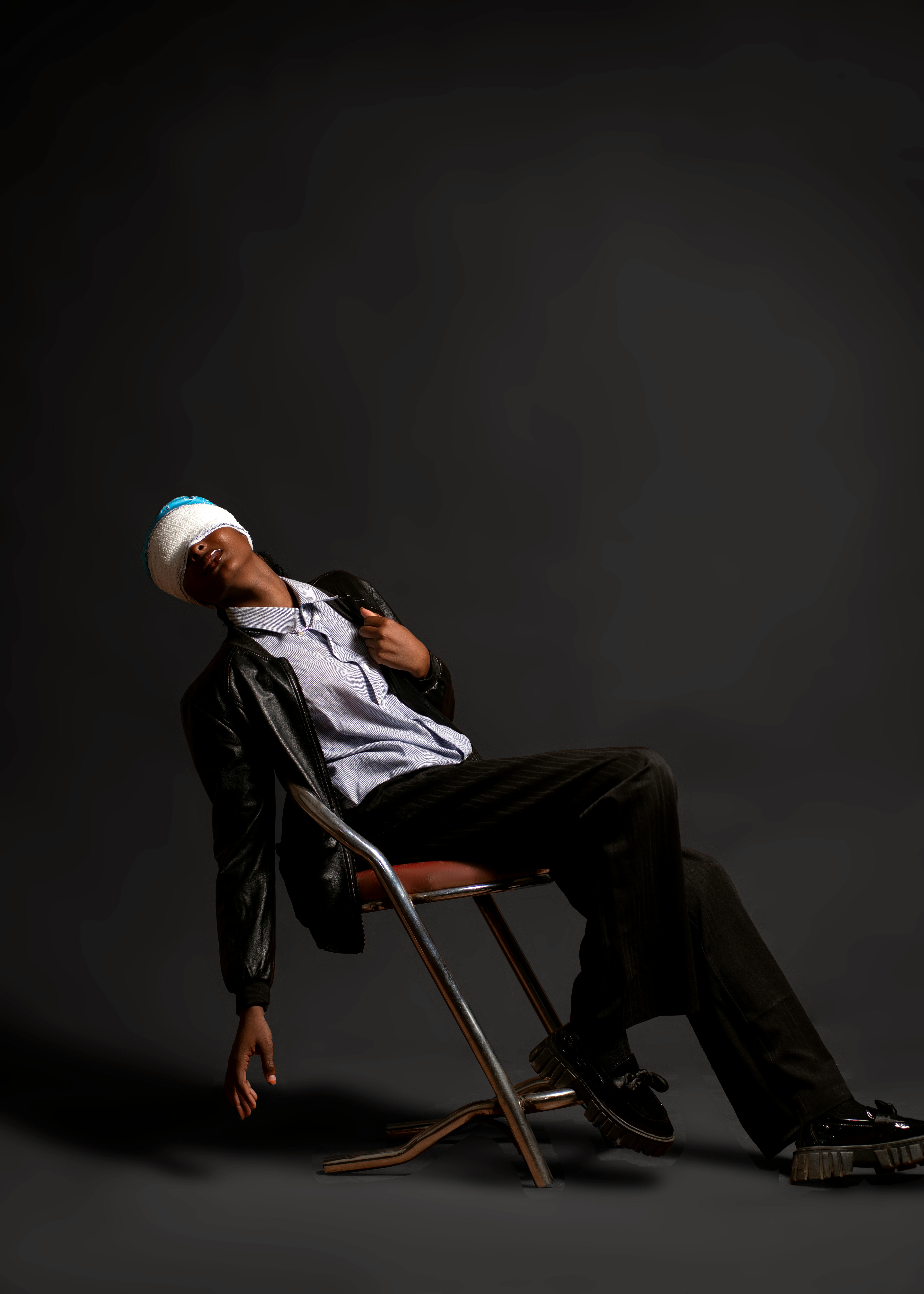 grátis Um jovem em traje casual está recostado em uma cadeira contra um fundo escuro. Foto profissional