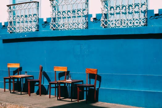 An outdoor cafe with wooden chairs and a blue wall under ornate windows in bright sunlight.